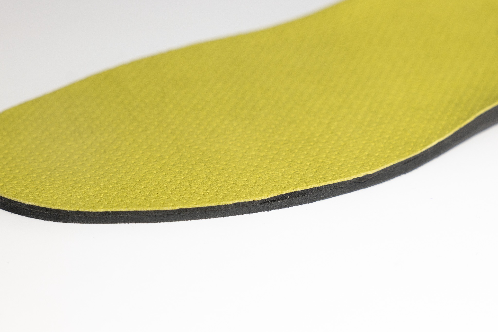 Żółto-czarna wkładka ortopedyczna z bliska, ukazująca teksturę i warstwową konstrukcję na białym tle. Wkładka jest częściowo widoczna, z wyraźnym detalem krawędzi.