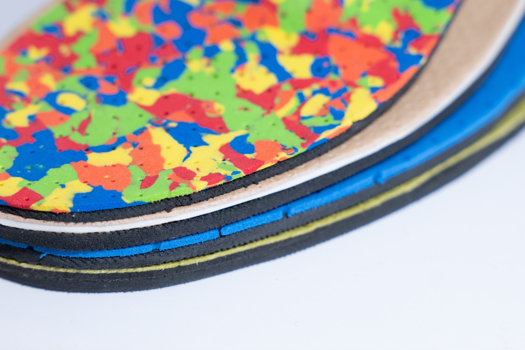 Wielobarwne, warstwowe wkładki ortopedyczne z pianki, ułożone jedna na drugiej, ukazujące strukturę i różnorodność materiałów. Makro zbliżenie na detale.