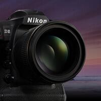 Czarny aparat fotograficzny Nikon z dużym obiektywem na tle rozmytego, fioletowo-pomarańczowego nieba o zmierzchu.