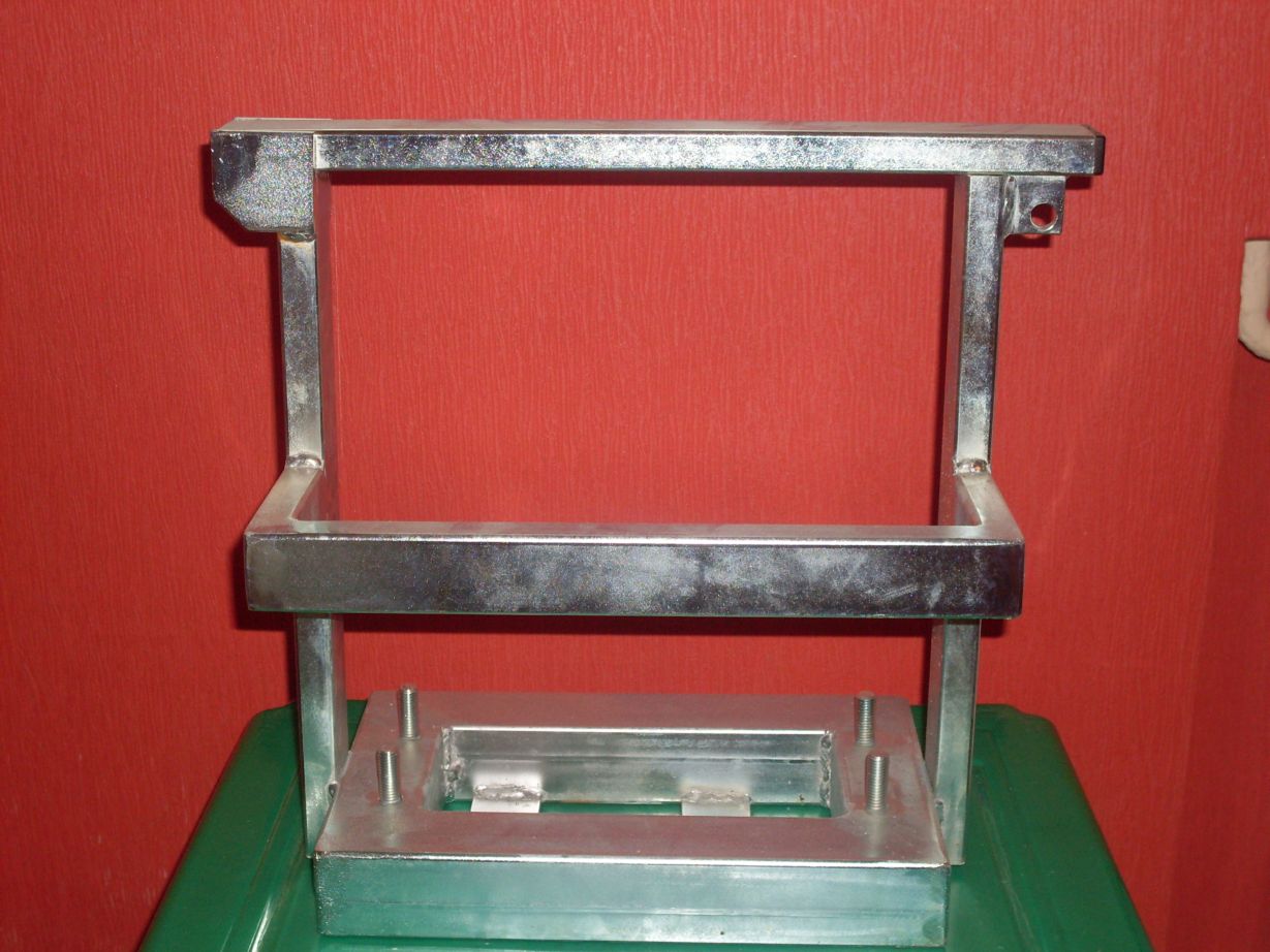 Metalowy stelaż zabezpieczenia FAAC, spawany z profili zamkniętych, widoczne spawy, otwór montażowy, całość na zielonym podłożu, czerwone tło.