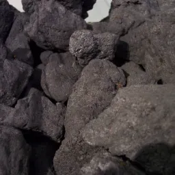 Koks: fragment stosu brył koksu o chropowatej, matowej powierzchni w odcieniach szarości, z widocznymi refleksami światła na niektórych powierzchniach.