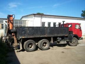 Czerwony samochód ciężarowy Kamaz z pomarańczowym HDSem na tle białego budynku z oknami.