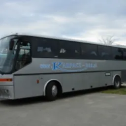 Srebrny autokar z napisem 'KARPACZ-BUS, przewóz osób' na boku, zaparkowany na żwirowym parkingu przy pochmurnym niebie.
