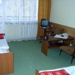 Pensjonat Amelia - Pokój w sanatorium w Iwoniczu Zdroju z dwoma pojedynczymi łóżkami z czerwonymi narzutami, stolikiem kawowym, telewizorem i fotelem. Widok na okno z zasłonami.