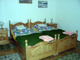Pokój dwuosobowy w pensjonacie w Iwoniczu Zdroju: dwa pojedyncze łóżka z drewnianymi ramami, zielone koce i kolorowe kołdry, dywaniki przy łóżkach, szafki nocne z lampkami.