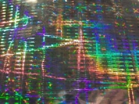 Holograficzna folia z motywem złotniczym, ukazująca rozproszone światło w tęczowych barwach, z widocznymi drobnymi, powtarzalnymi wzorami i napisami.