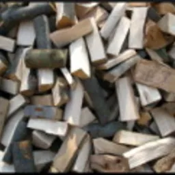 Stos pociętego drewna opałowego, jasne i ciemne kawałki ułożone chaotycznie, widoczne słoje drewna.