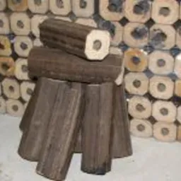 Ułożony stos brykietu drzewnego z otworem w środku, na tle zapakowanych paczek brykietu w przezroczystej folii.