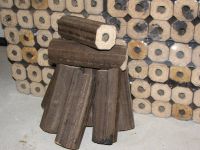 Ułożony stos brykietu drzewnego z otworem w środku, na tle zapakowanych paczek brykietu w przezroczystej folii.