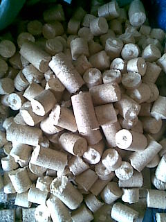 Stos okrągłych, jasnych briketów z widoczną strukturą włókien, ułożonych chaotycznie w nieokreślonym pojemniku lub na powierzchni.