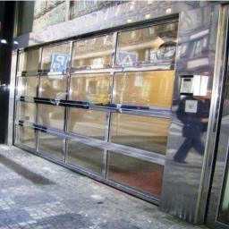 ROL-DOM rolety-bramy-żaluzje-markizy - Nowoczesna brama garażowa segmentowa ze stali nierdzewnej z przeszkleniami, widoczna z zewnątrz budynku, odbijająca otoczenie.