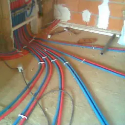 Rozprowadzenie instalacji grzewczej i wodnej w nowo budowanym domu, widoczne czerwone i niebieskie rury przymocowane do podłoża, ściany w trakcie budowy.