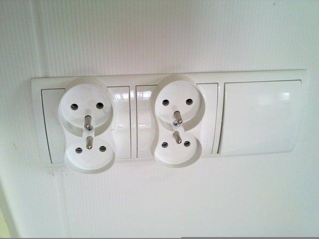 Dwa podwójne gniazdka elektryczne typu francuskiego (Schuko) zamontowane na białej ścianie, widoczne metalowe bolce uziemiające.