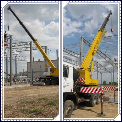 Montaż konstrukcji stalowej hali z użyciem dźwigu samojezdnego, widoczni pracownicy na wysokościach, teren budowy w trakcie prac ziemnych.