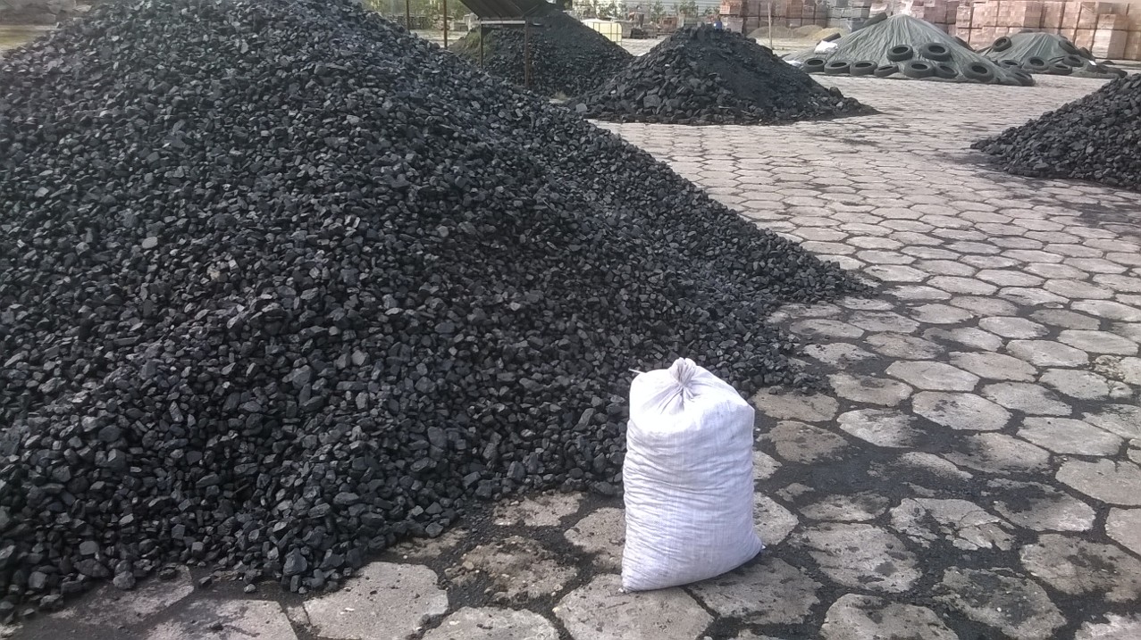 Góra węgla orzech II na placu składowym z workiem obok, widoczne inne pryzmy w tle.