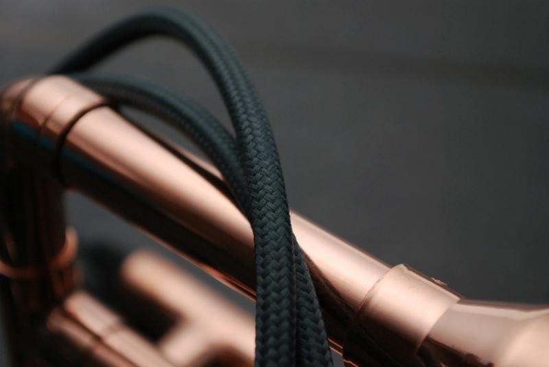 Miedziana lampa z czarnym, plecionym kablem w zbliżeniu, industrialny design.