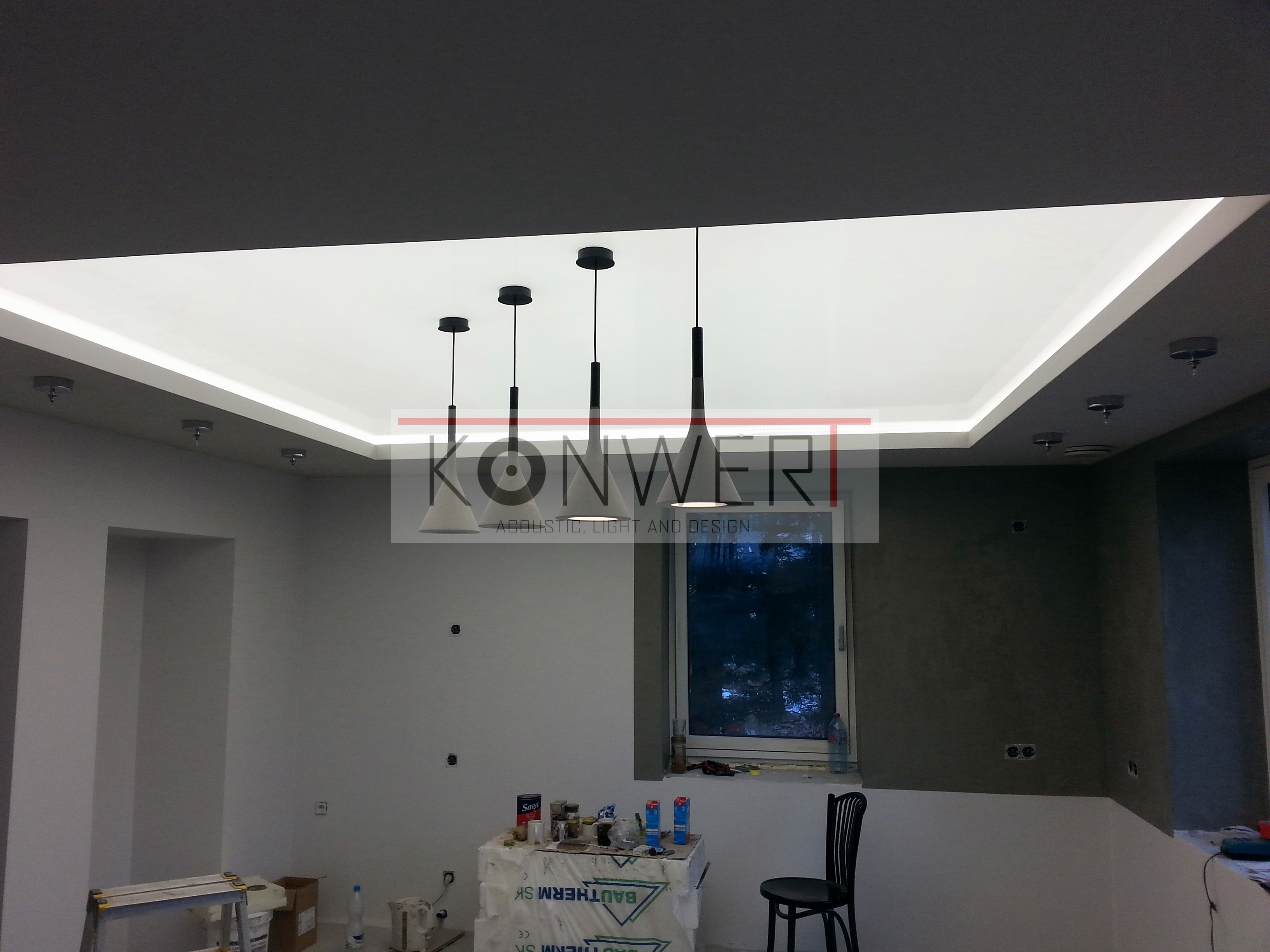 Wnętrze w trakcie remontu z trzema nowoczesnymi lampami wiszącymi o stożkowych kloszach, zamontowanymi w podwieszanym suficie z oświetleniem LED, widoczne puszki elektryczne w ścianie, okno...