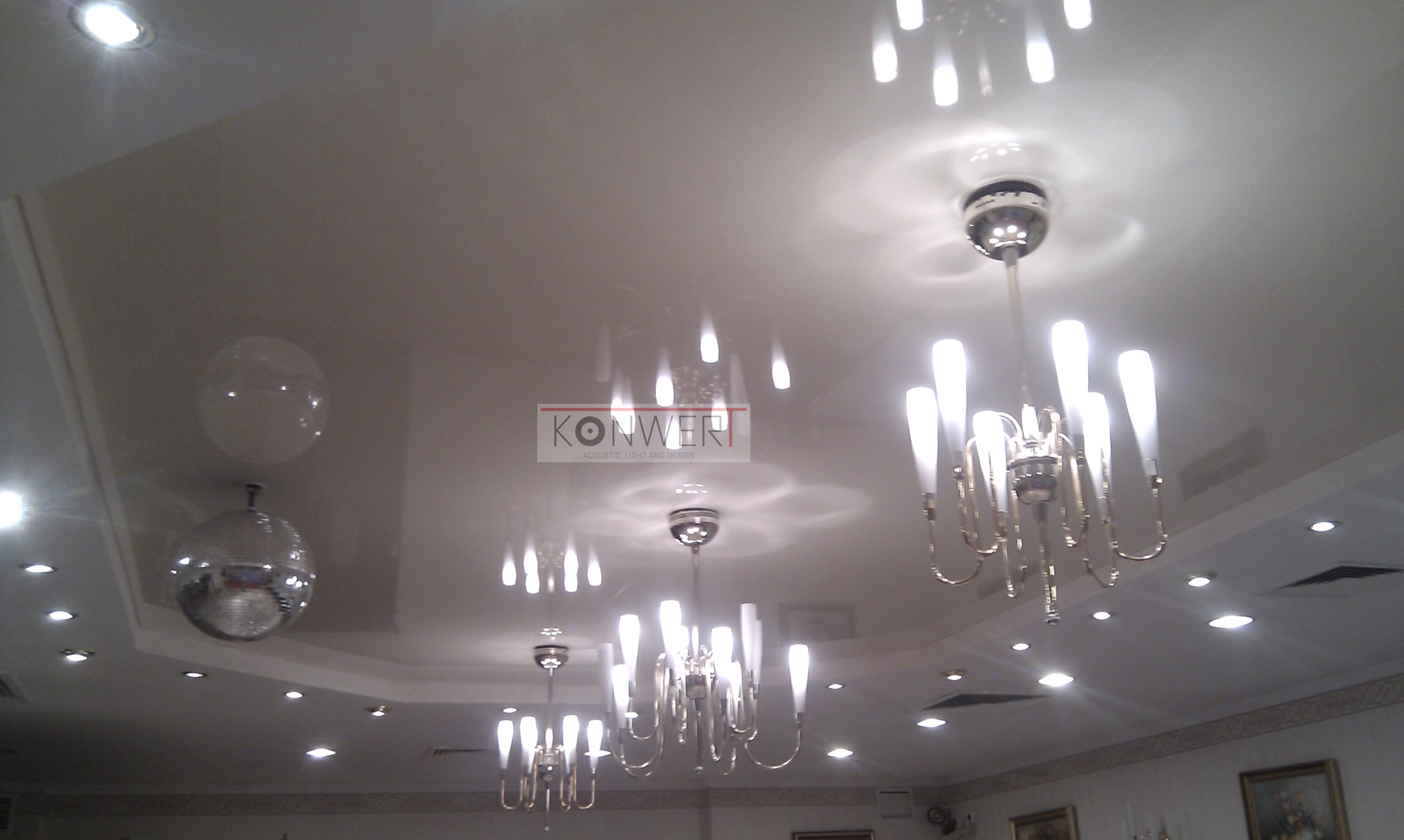 Błyszczący sufit napinany z refleksami, oświetlony kilkoma żyrandolami w stylu retro i kulą dyskotekową, widok z dołu.