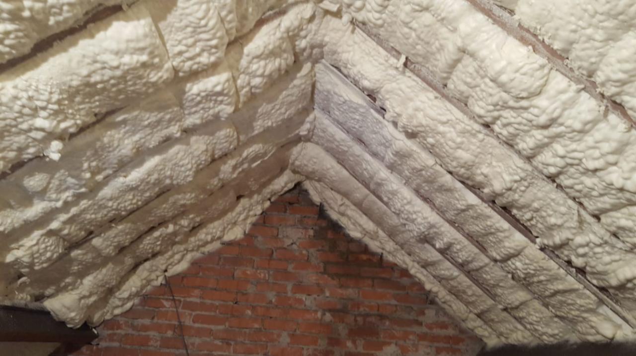 Poddasze z drewnianą konstrukcją dachu po izolacji natryskowej, widoczny fragment muru z czerwonej cegły.