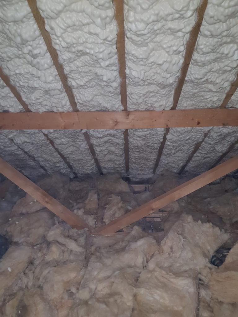 Poddasze z widoczną izolacją: biała pianka na krokwiach i wełna mineralna na ścianach szczytowych.
