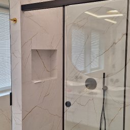 Pil-dom,Paweł Subotkiewicz - Nowoczesna kabina prysznicowa z przesuwnymi drzwiami w łazience wyłożonej płytkami imitującymi marmur z złotymi żyłami, z czarną armaturą i oświetleniem LED w suficie.