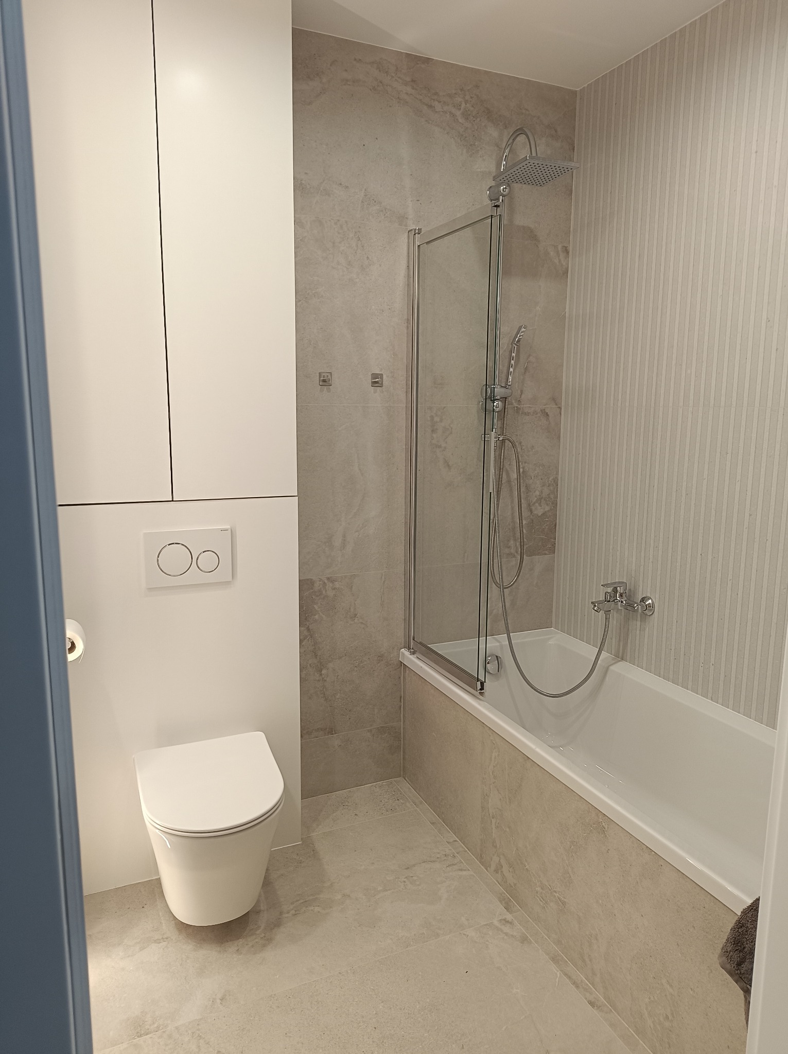 Nowoczesna łazienka z wanną, szklanym parawanem, podwieszaną toaletą i szarą płytką imitującą marmur na ścianach i podłodze. Minimalistyczny design.