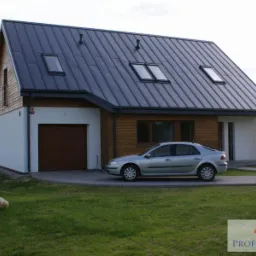 Nowoczesny dom z drewnianą elewacją i ciemnym dachem, z trzema oknami dachowymi, garażem z brązową bramą i srebrnym samochodem na podjeździe.