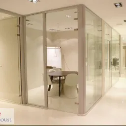 Szklane ścianki działowe tworzące nowoczesne biuro z widoczną salą konferencyjną i białymi krzesłami. Jasna podłoga odbija światło, zwiększając wrażenie przestronności.