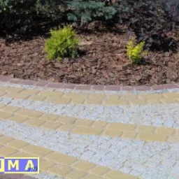 Obrzeże rabaty z kory i niskich roślin, wykończone kostką brukową w kolorach żółtym i szarym, zrealizowane w Rudzie Śląskiej.