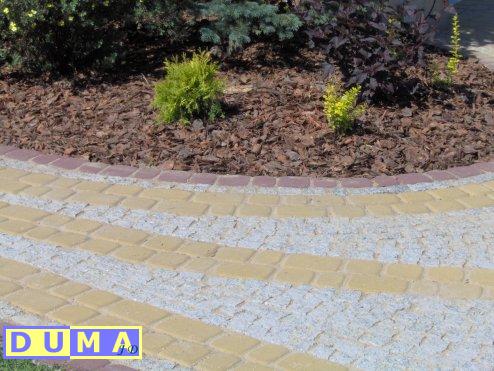 Obrzeże rabaty z kory i niskich roślin, wykończone kostką brukową w kolorach żółtym i szarym, zrealizowane w Rudzie Śląskiej.