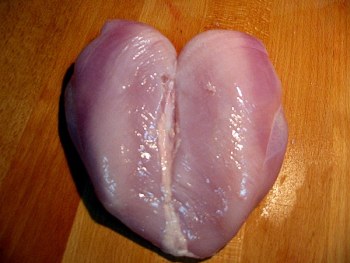 Surowy filet z kurczaka ułożony na desce do krojenia, widoczne włókna mięsa i delikatny połysk.