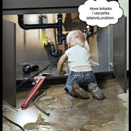 Wiercenie studni Legionowo Białołęka zainstal - Mały blond chłopiec klęczy przed szafką pod zlewem, przyglądając się instalacji hydraulicznej, z rozwartym kluczem i wężem na podłodze, która jest zalana wodą, a nad głową chłopca znajduje się...