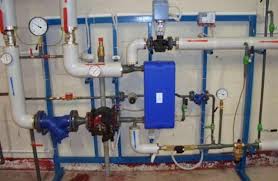 Instalacja hydrauliczna z rurami, zaworami, manometrami i niebieskim zbiornikiem, zamontowana na ścianie z widocznymi elementami mocującymi.