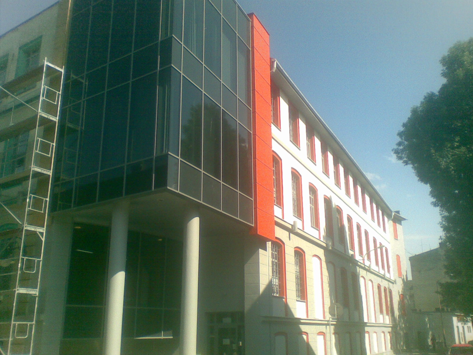 Budynek biurowy z nowoczesną szklaną fasadą i fragmentem odnowionej elewacji w kolorze białym z czerwonymi obramowaniami okien, widoczne rusztowanie.