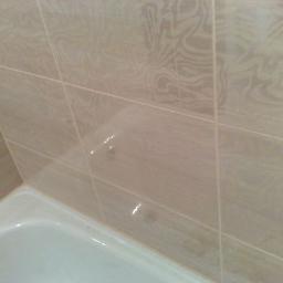 Fest Usługi - Fragment łazienki z beżowymi, wzorzystymi płytkami ceramicznymi na ścianie nad białą wanną z widocznym odpływem.