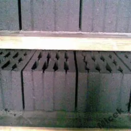 Szare pustaki żużlowe ułożone w rzędach, oddzielone drewnianymi listwami, widoczne charakterystyczne otwory w strukturze.