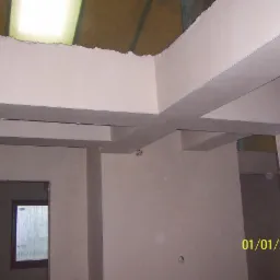 Surowe wnętrze z nałożonymi jasnymi tynkami na ścianach i suficie, widoczne elementy konstrukcyjne i otwory okienne, całość w trakcie wykończenia.