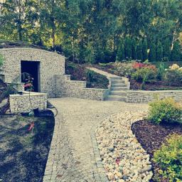 Bruk-Master - Ogród z kamienną ścieżką, schodami i piwniczką ziemną z kamienia, otoczony zielenią i drzewami.