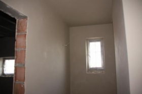 Świeżo położone, gładkie tynki kwarcowe w pomieszczeniu w Nowym Sączu, przygotowane pod malowanie. Widoczna surowa ościeżnica drzwiowa z cegły.