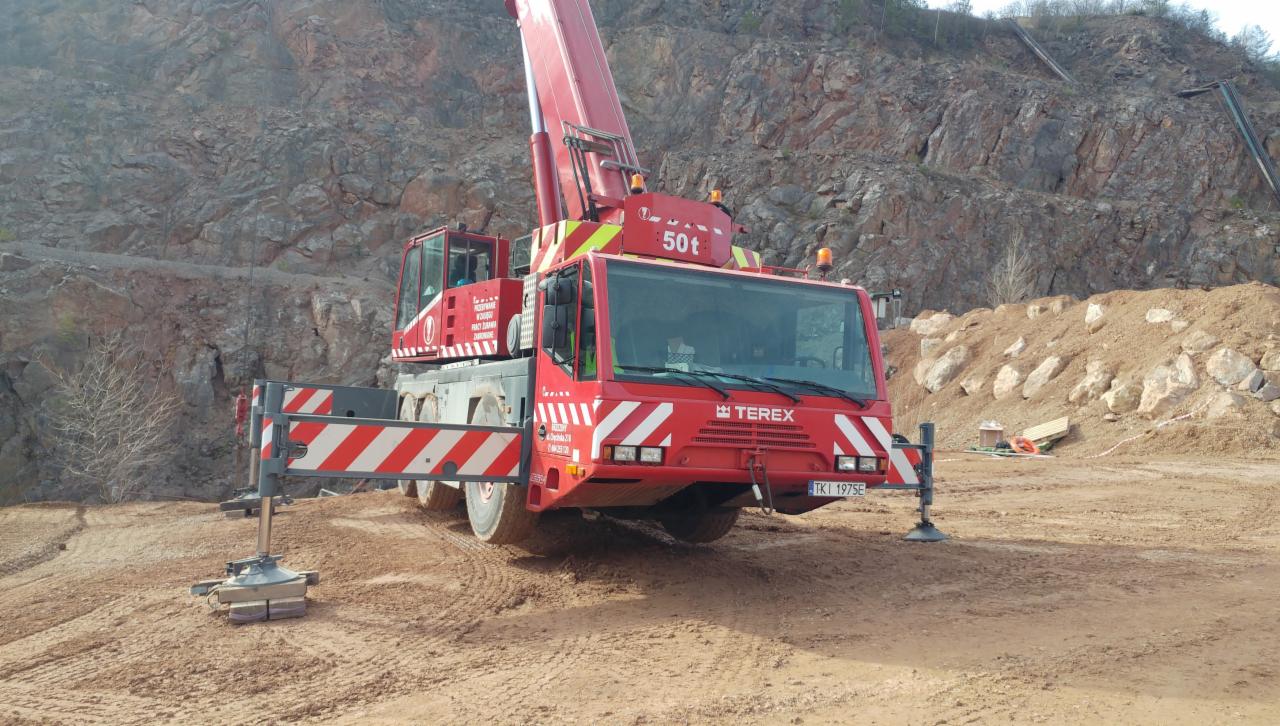 Czerwony dźwig samochodowy marki Terex o udźwigu 50 ton, z wysuniętym ramieniem, ustawiony na placu budowy w Brzezinach na tle skalistej ściany kamieniołomu.