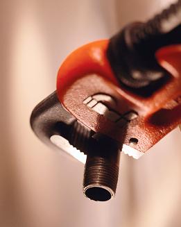 Czerwony klucz hydrauliczny chwyta gwintowaną rurę w zbliżeniu, widoczne ślady użytkowania na narzędziu, miękkie, rozproszone światło.