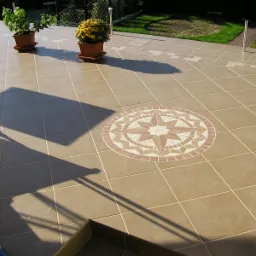 Beżowa, kwadratowa płytka ceramiczna na tarasie z dekoracyjnym motywem rozety w centrum, doniczki z roślinami w tle