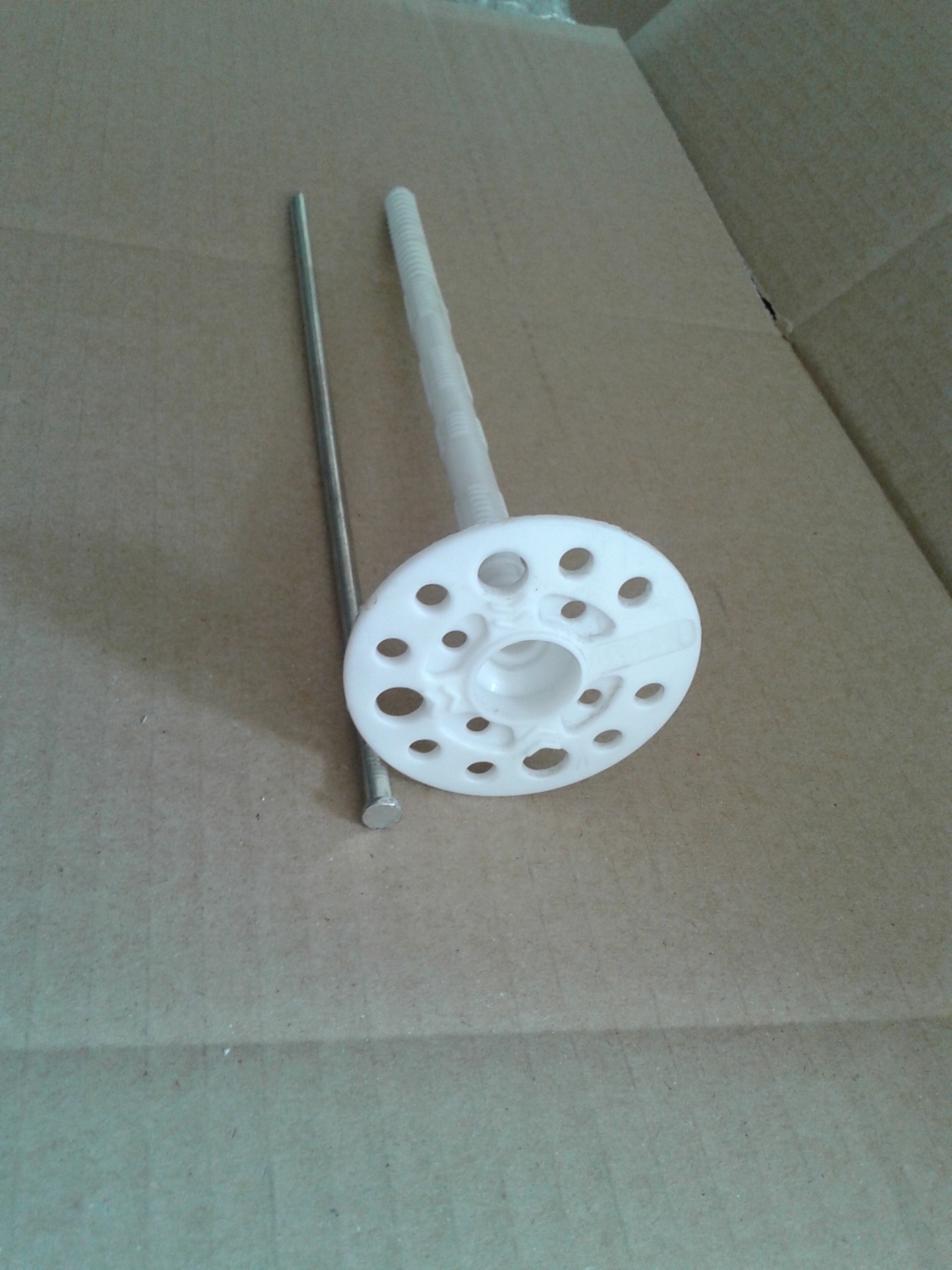 Pojedynczy, biały kołek do styropianu z metalowym trzpieniem, widoczny na kartonowym tle w Dąbrowie Górniczej.