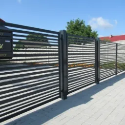 Nowoczesne ogrodzenie posesji z poziomych paneli w kolorze antracytowym, skrzynka pocztowa z napisem 'Listy' i 'Gazety', kostka brukowa na podjeździe.