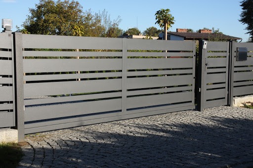 Nowoczesna, przesuwna brama w kolorze grafitowym z poziomymi szczelinami, zamontowana na posesji z brukowaną nawierzchnią i skrzynką pocztową.