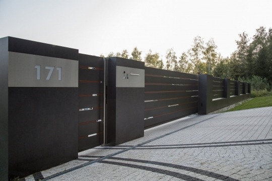 Nowoczesna, przesuwna brama wjazdowa z numerem domu 171, wykonana z ciemnego metalu z poziomymi, wąskimi prześwitami, na tle kostki brukowej i zieleni.