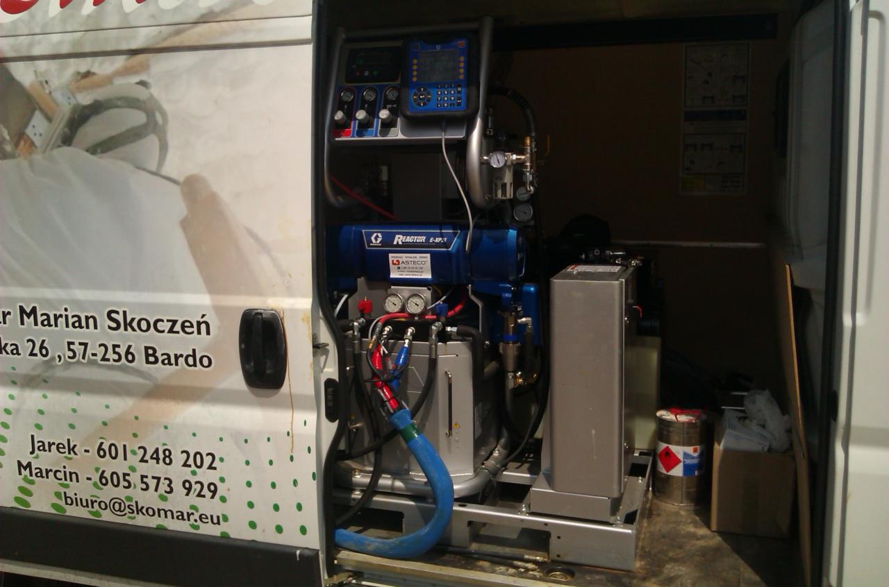 Sprzęt natryskowy Reactor E-XP1 Asteco w furgonetce, używany do izolacji natryskowej, z widocznymi przewodami i elementami sterującymi.