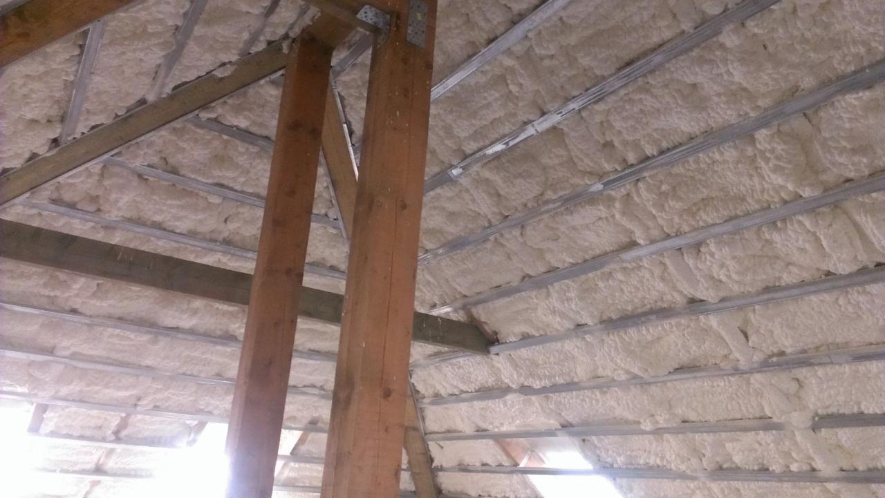 Poddasze z widoczną pianką izolacyjną między krokwiami i metalowymi profilami. Drewniane słupy konstrukcyjne na pierwszym planie.