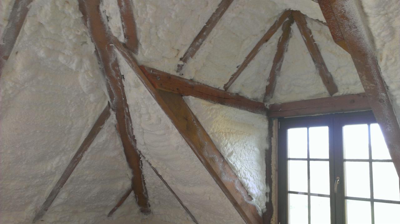 Poddasze z drewnianą konstrukcją pokryte białą pianą izolacyjną, widoczne okno. Izolacja natryskowa poddasza.