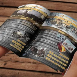 Rozłożona broszura reklamowa z ofertą tematycznych wycieczek i programów edukacyjnych w stylu Dzikiego Zachodu, trzymana w dłoniach na tle drewnianego stołu.